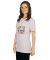 Smiling woman wearing a light pink t-shirt with colorful Just here to make it weird text on front.